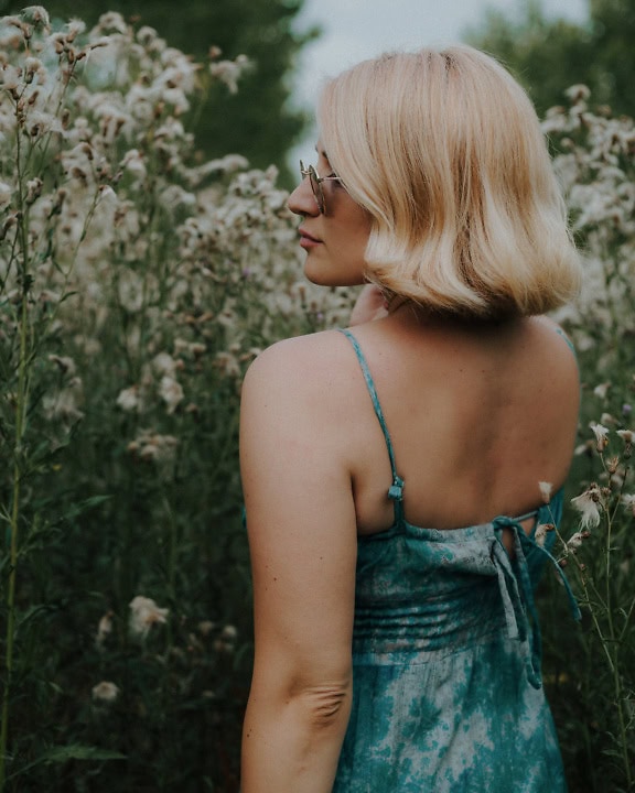 Portrait d’une belle jeune blonde de dos tourné dans une robe à bretelles dans un champ de fleurs