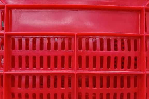 Povrch tmavě červeného plastového koše s otvory