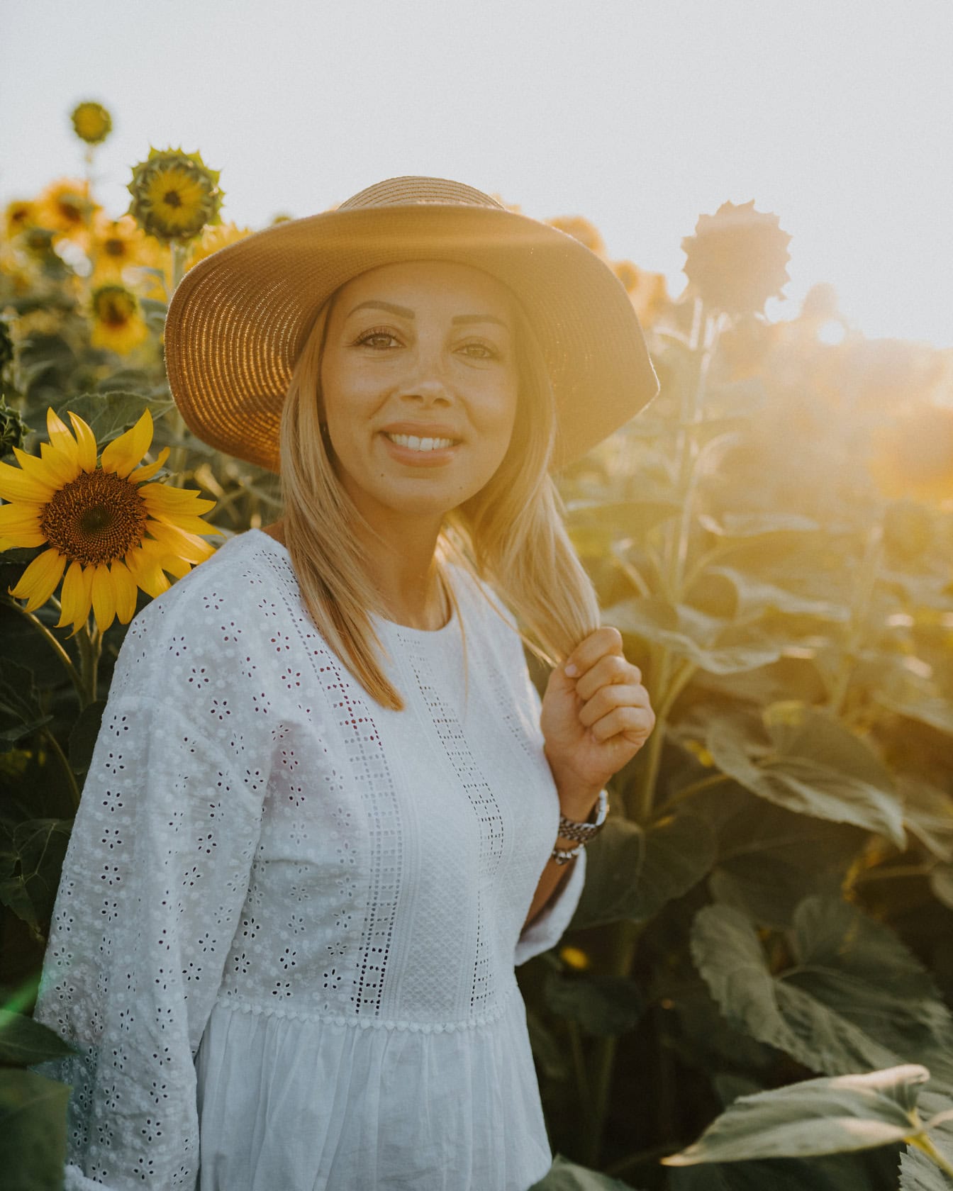 Portrét usmievavého vidieckeho dievčaťa v slamenom klobúku v slnečnicovom poli s jasným slnečným svetlom ako podsvietením