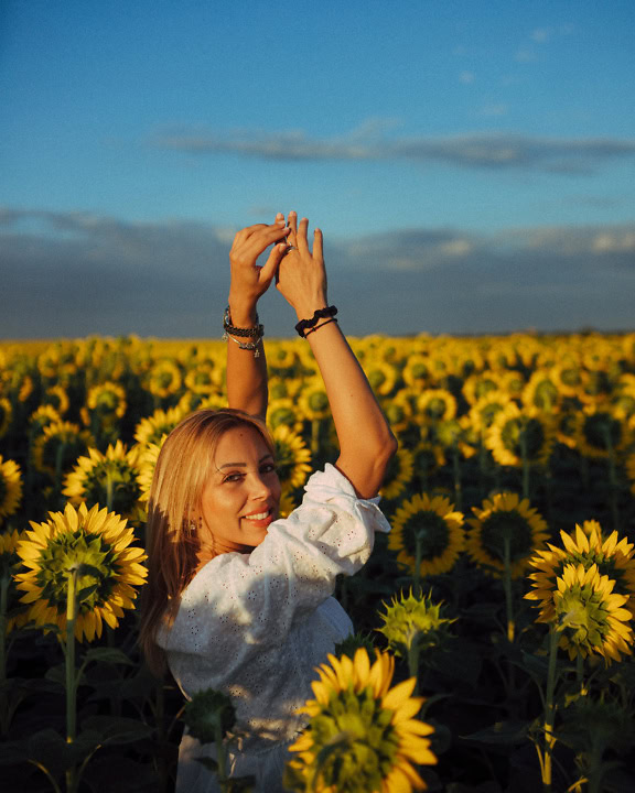 Porträtt av en glad och leende lantflicka i ett solrosfält med hennes händer upphöjda