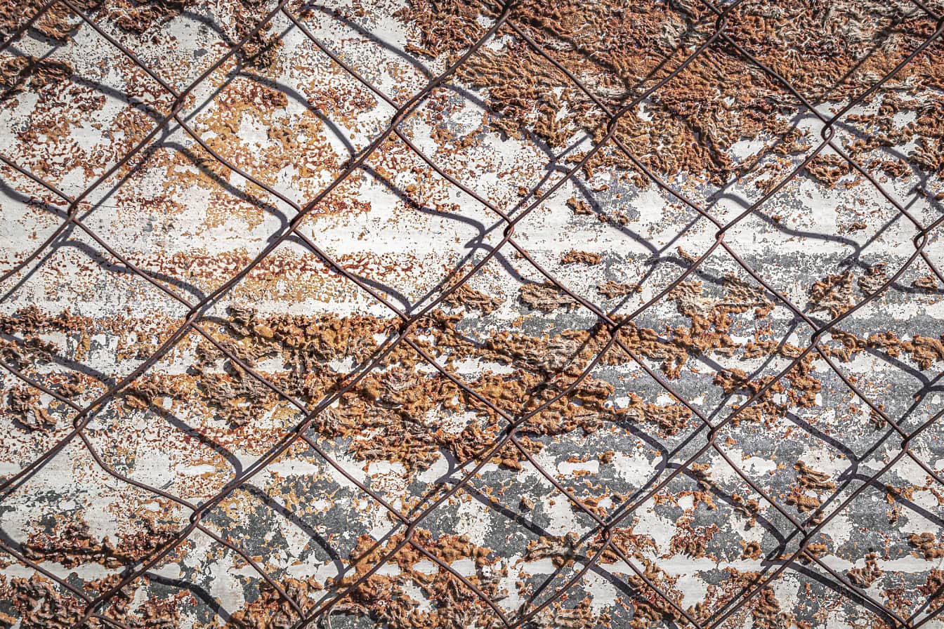 Textúra pozinkovaného kovu so stopami izolačnej peny na ňom s drôteným plotom nad ním