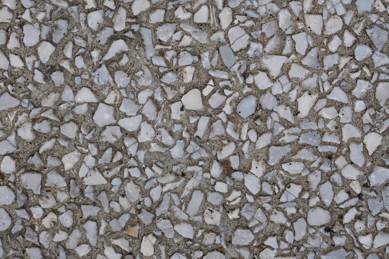 Textura de fragmentos de pedras de granito branco-acinzentado em superfície de concreto