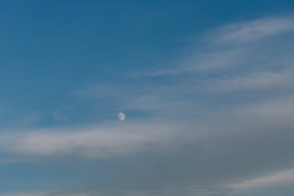 Синьо небе с мъгливи облаци и малка бяла луна в далечината