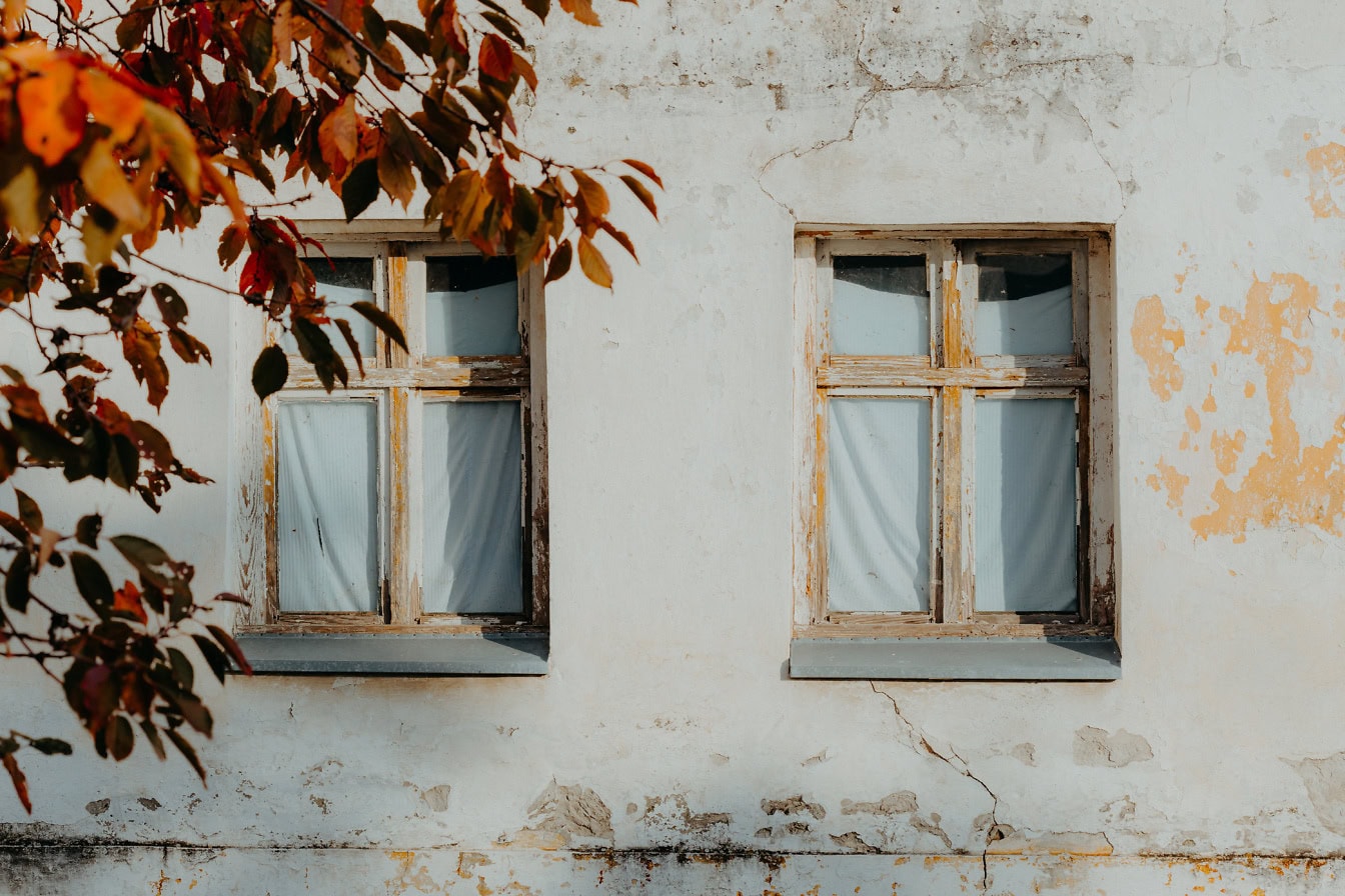 Δύο ξύλινα παράθυρα στον βρώμικο λευκό τοίχο του παλιού σπιτιού