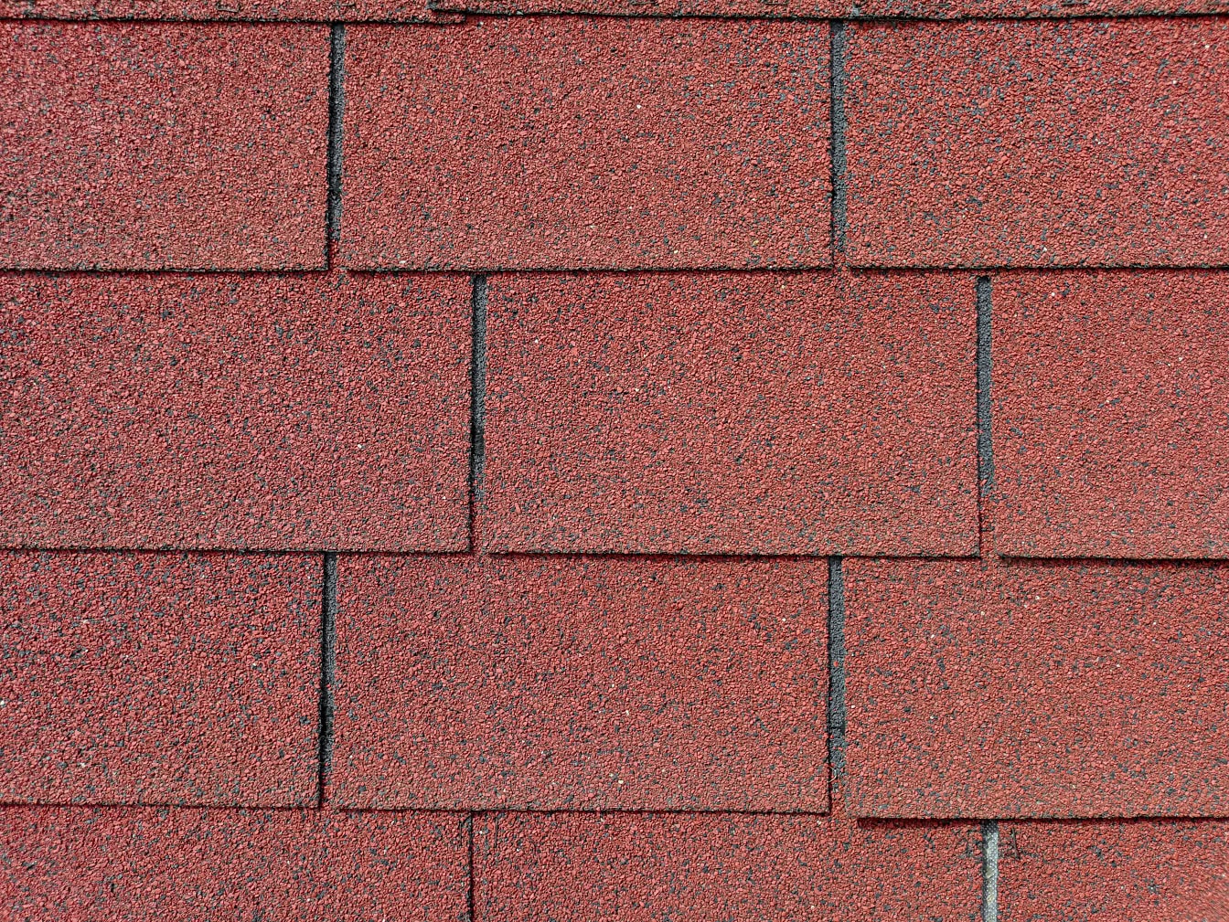 Texture of a dark reddish-brown shingle roof of rectangular shape made of mix of bitumen, rubber and recycled plastic