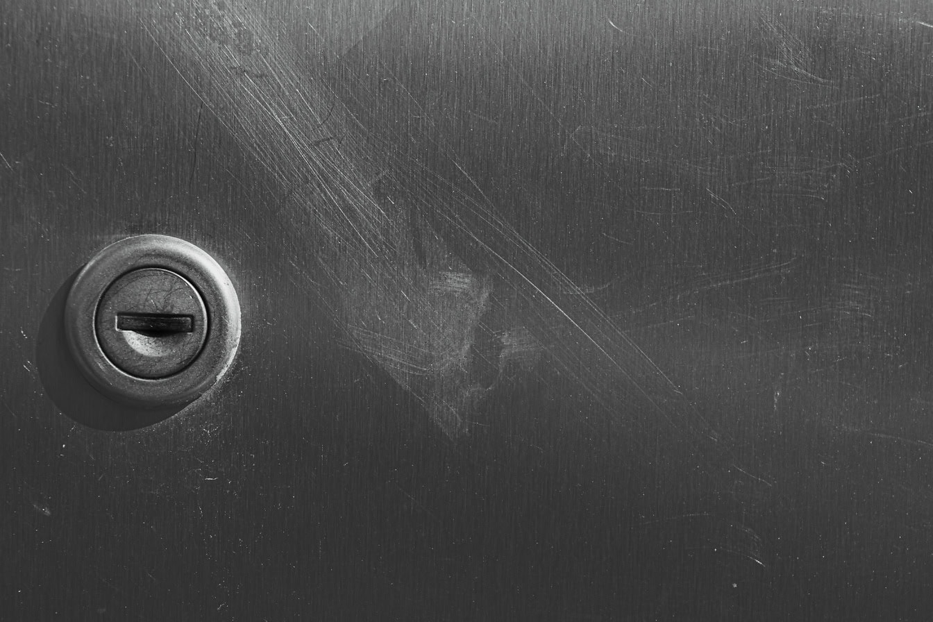 Close-up of a keyhole on scratched stainless steel metal sheet texture