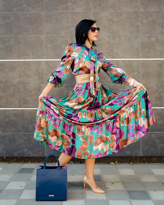 Kvinna poserar i färgrik sidenklänning medan hon håller klänning med utsträckta armar