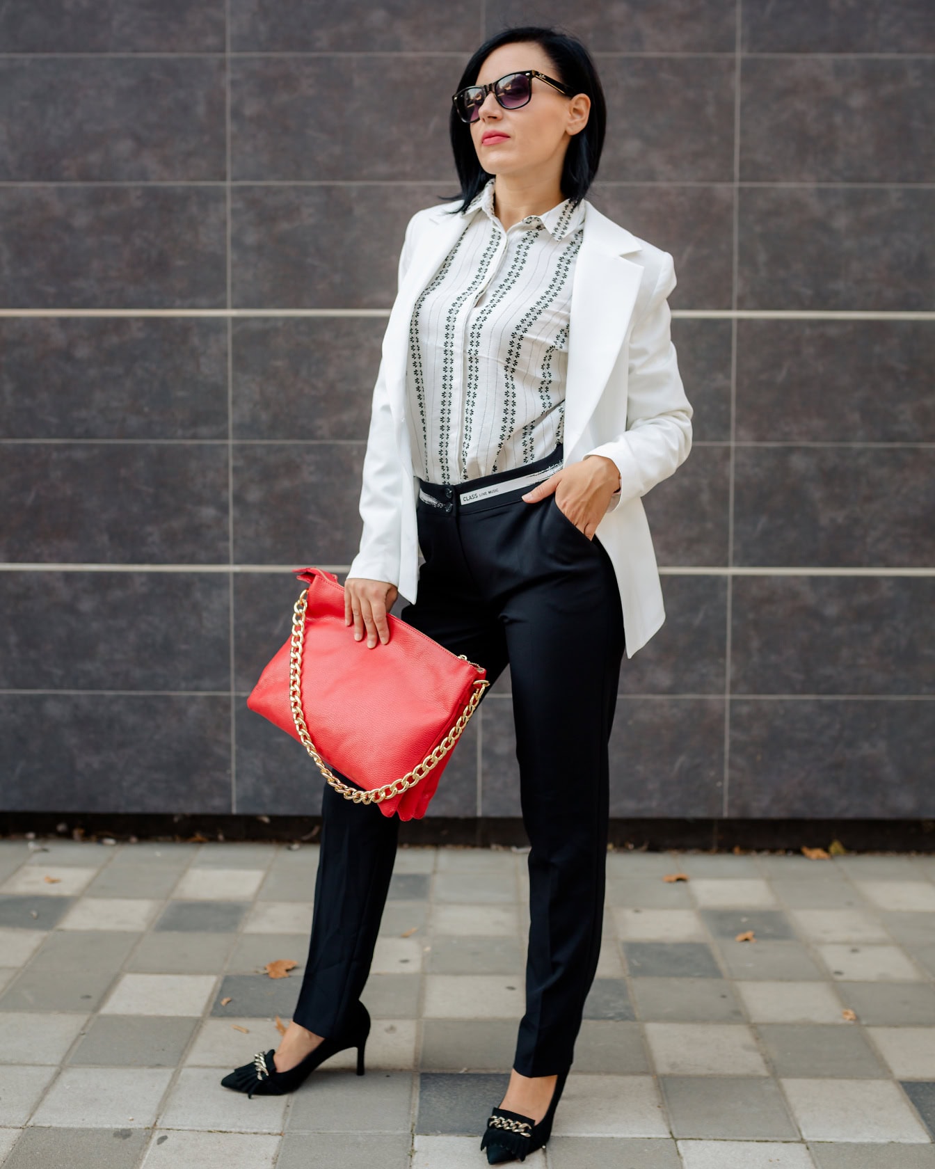 Hübsche Geschäftsfrau posiert in einem schwarz-weißen Anzug mit einer roten Handtasche mit goldenem Kettengriff