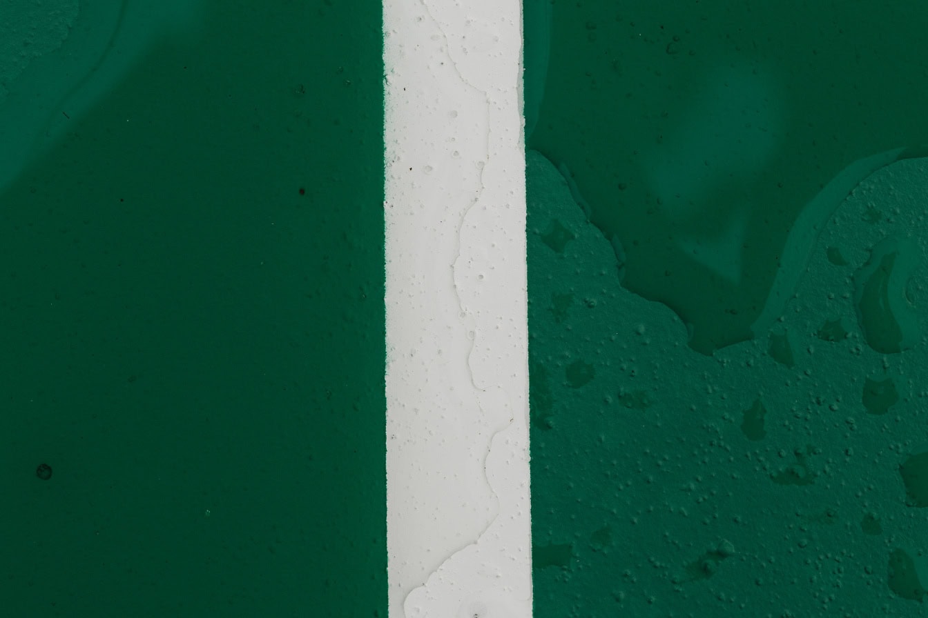 เส้นสีขาวแนวตั้งตรงกลางพื้นผิวสีเขียวเข้มเปียก