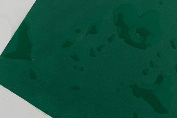 Mørkegrønn og hvit maling på metallplate med vanndråper
