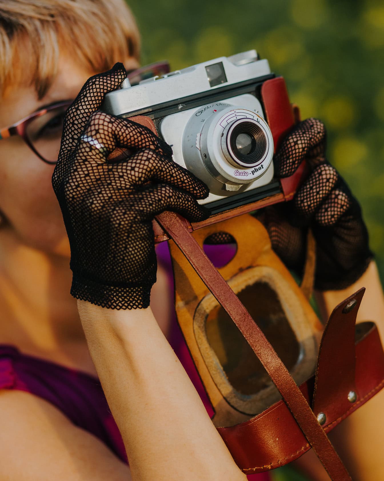 Tyylikkäisiin pitsihansikkaisiin pukeutunut nainen pitelee vanhaa analogista kameraa