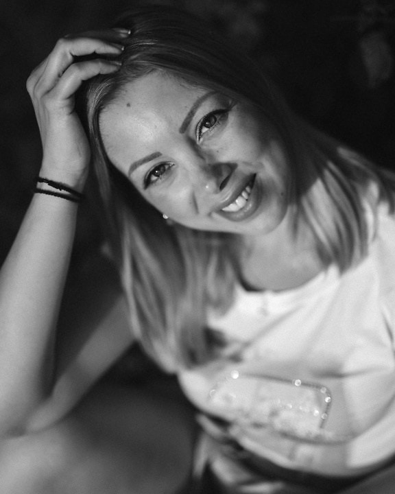 Portret alb-negru al unei tinere frumoase zâmbitoare, cu mâna pe cap