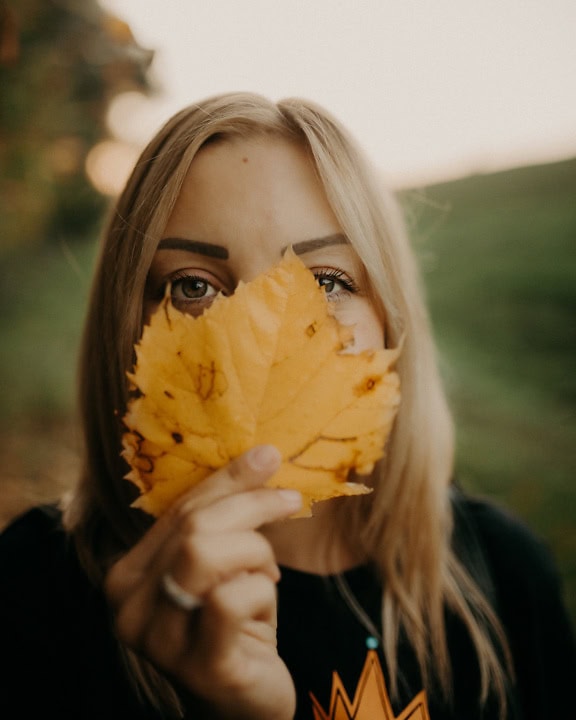 Porträtt av en blond kvinna som håller ett gulaktigt blad över hennes ansikte