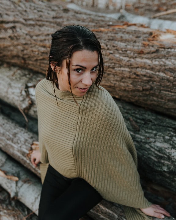 Portrét pohledné brunetky v ručně pleteném svetru při pózování opřené o klády