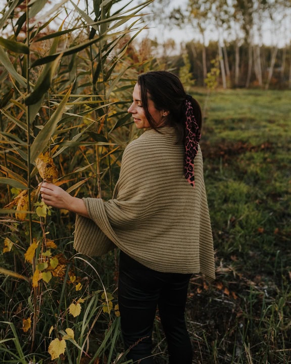 Портрет на жена в ръчно изработено пончо стои в поле до тръстиките