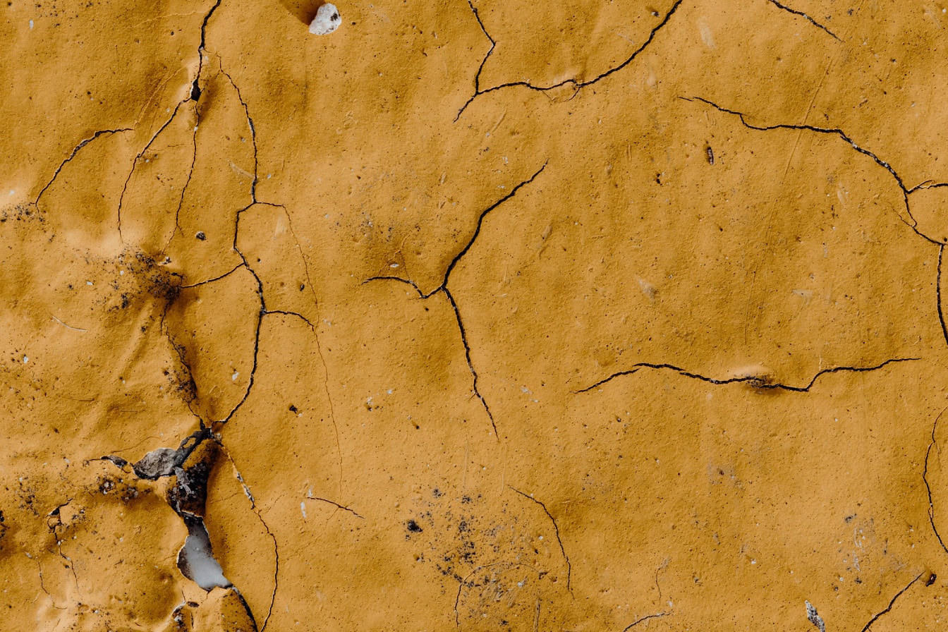 The texture of the cracked wall with yellowish brown lime paint peeling off the surface