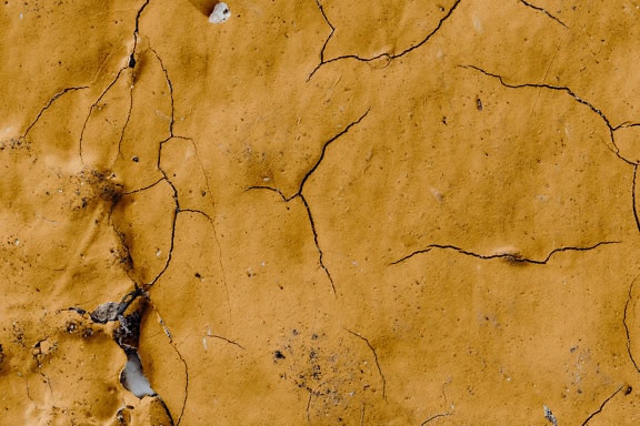 Teksturen til den sprukne veggen med gulbrun kalkmaling som skreller av overflaten