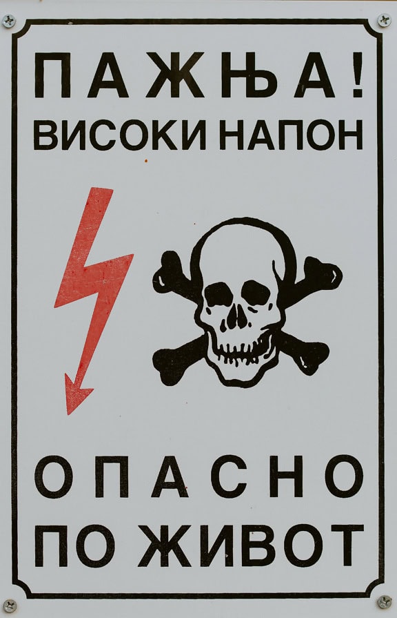 Cartello di avvertimento con teschio e ossa incrociate e fulmine e con lettere cirilliche con iscrizione ad alta tensione elettrica