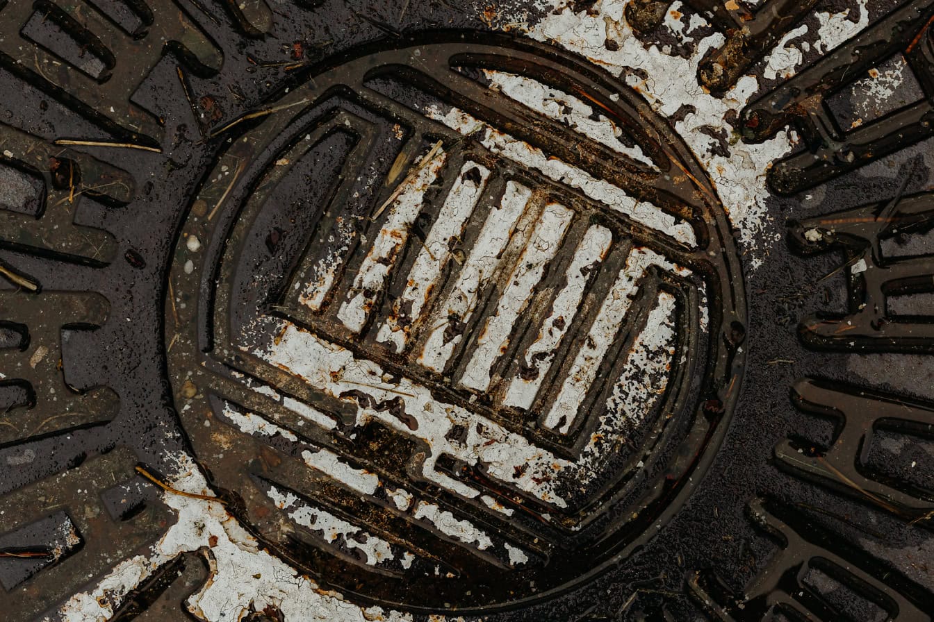 녹슬고 젖은 맨홀 뚜껑의 질감과 주철에서 벗겨진 오래된 흰색 페인트의 흔적