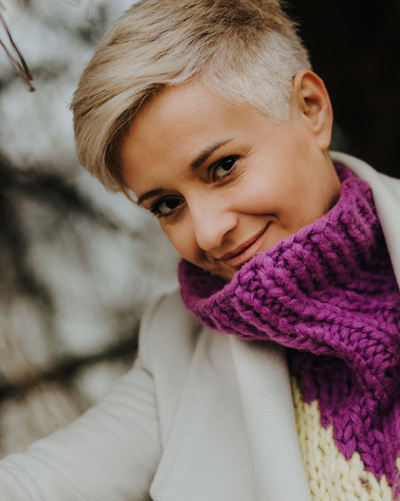 Portrait of a blonde with short hair wearing purple hand-woven sweater under a white coat