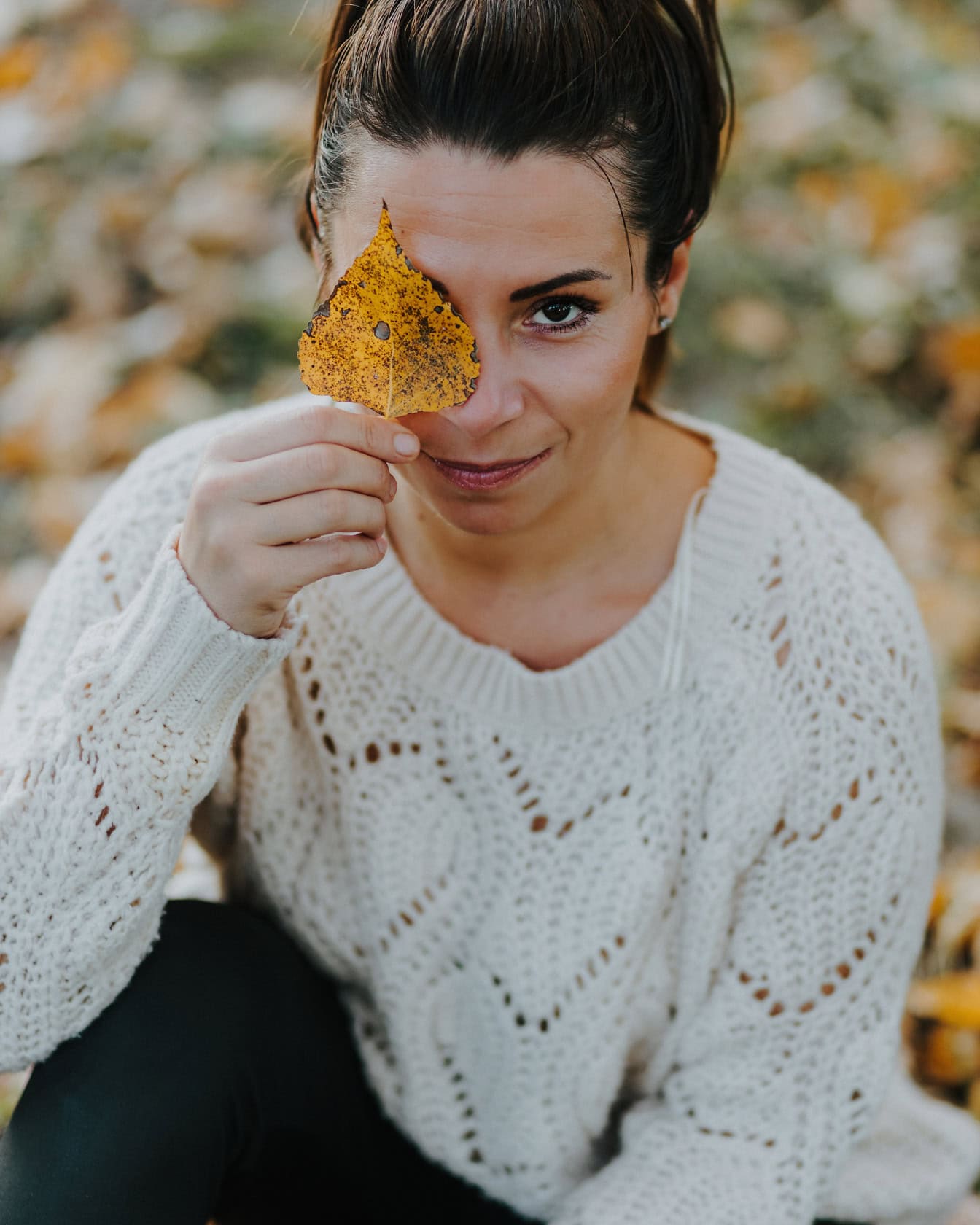 Portrait of young beautiful woman holding a leaf over her eye