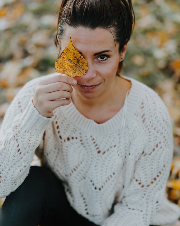 Portret de tânără femeie frumoasă ținând o frunză peste ochi