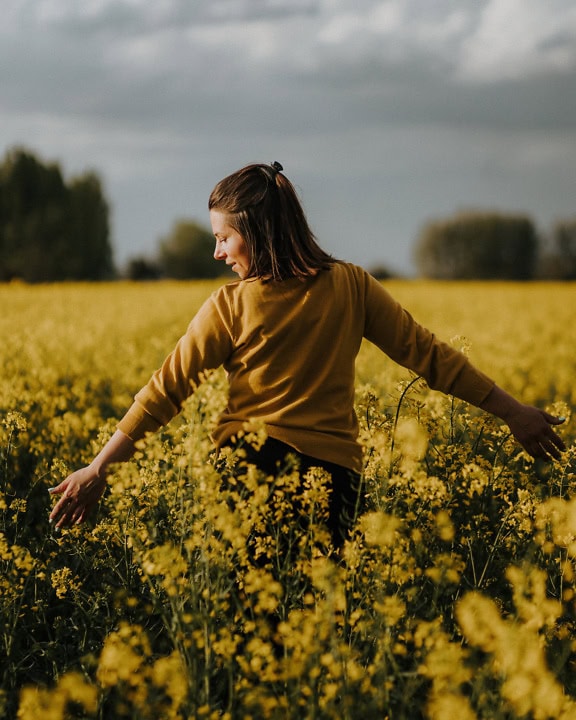 Uma jovem alegre está em um campo de flores amareladas e o toca de braços abertos
