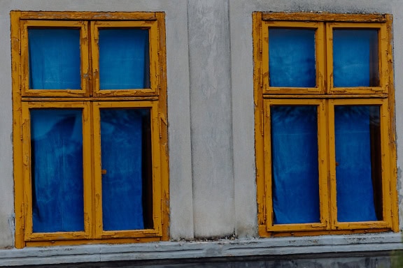 Două ferestre vechi din lemn maro-gălbui, cu perdele albastru închis