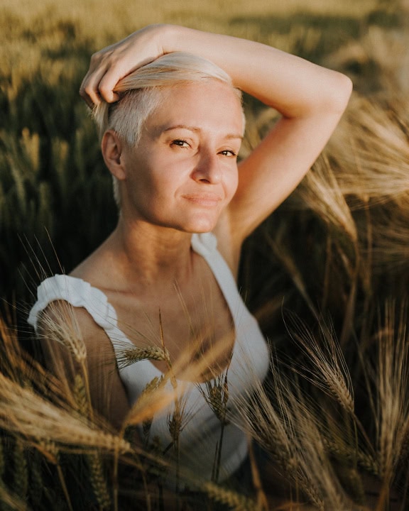 Una giovane donna con un taglio di capelli corto biondo posava con la mano tra i capelli in un campo di grano