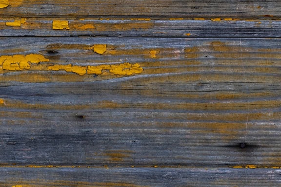 Texture of a wooden planks with old yellowish brown paint that peels off from the wood