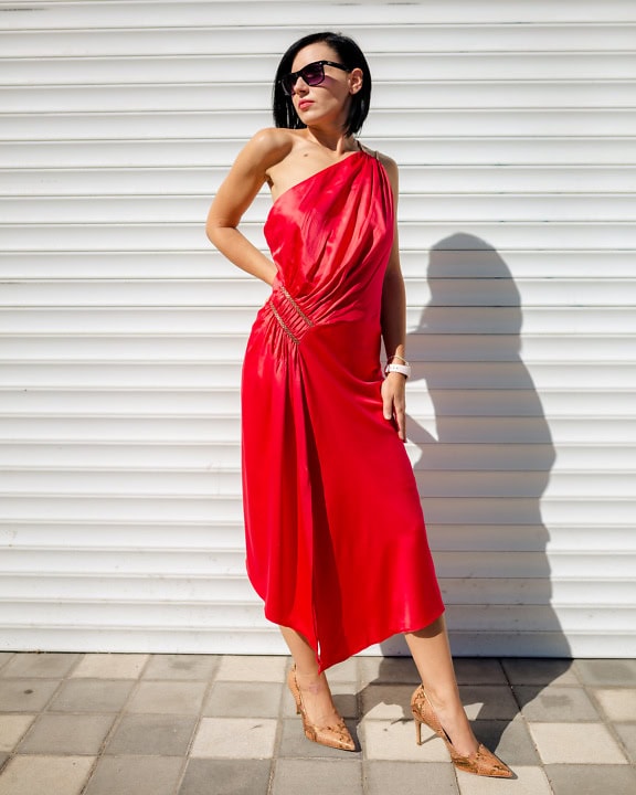 Mulher incrivelmente bonita e magra em um vestido vermelho elegante e sedutor ao lado da parede branca