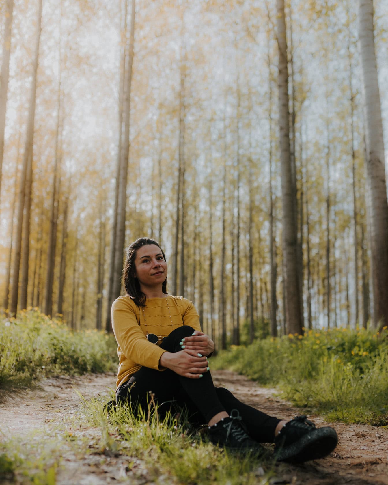 Potret seorang wanita muda yang riang duduk di jalan tanah di hutan