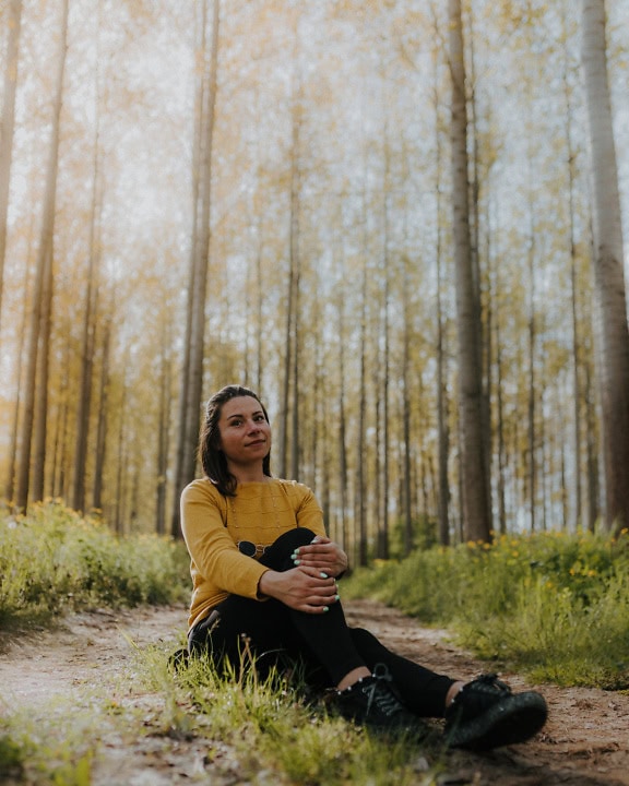 Porträt einer fröhlichen jungen Frau, die auf einem Feldweg in einem Wald sitzt