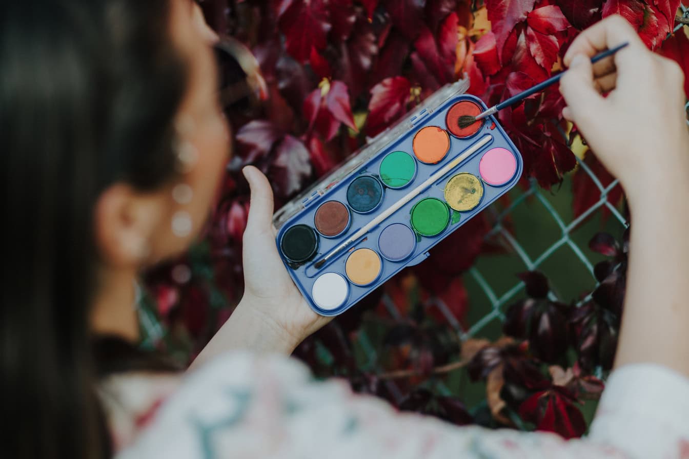 Akvarelová krabička, kterou drží malířka, zatímco používá štětec k rozmazání barvy
