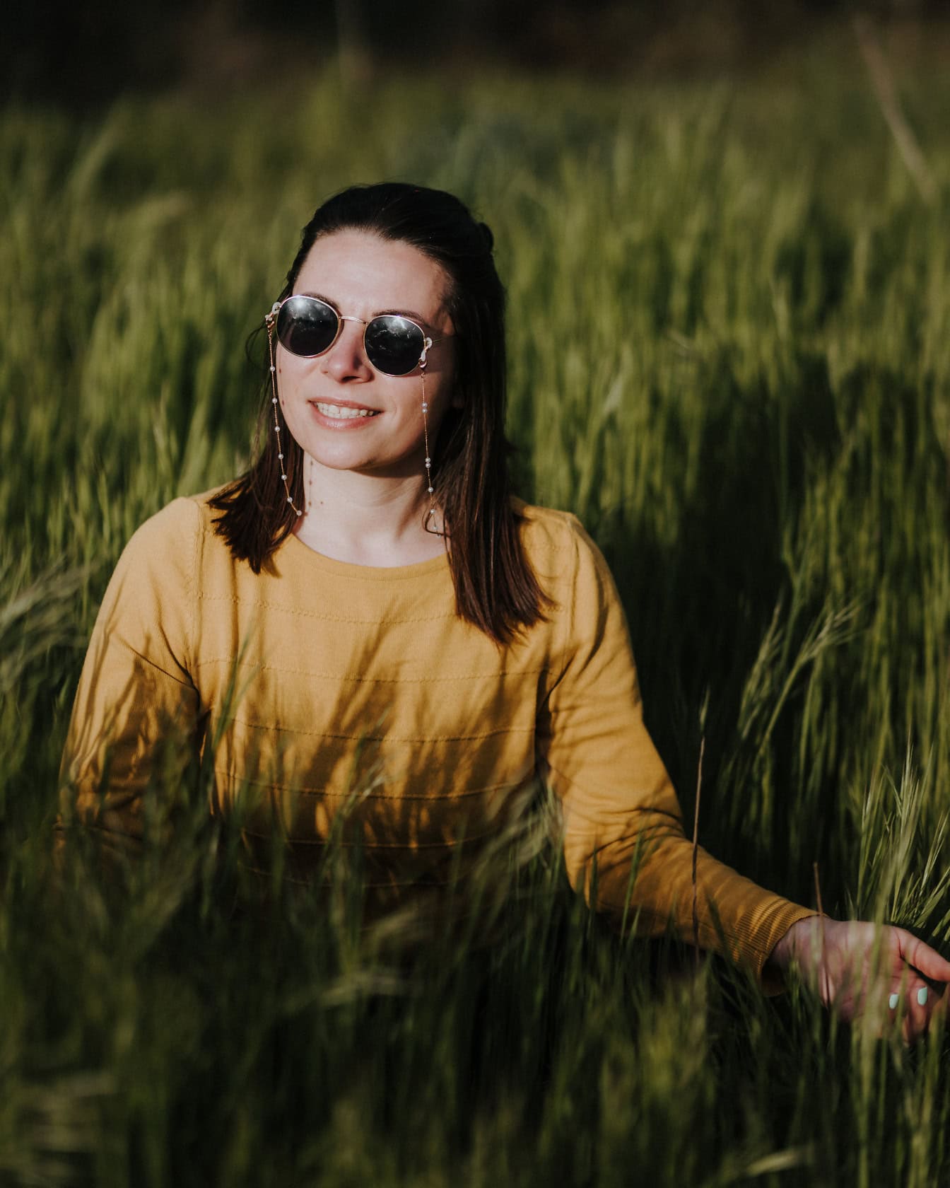 一个美丽的微笑女人的肖像，戴着约翰·列侬风格的太阳镜，在高高的草地上
