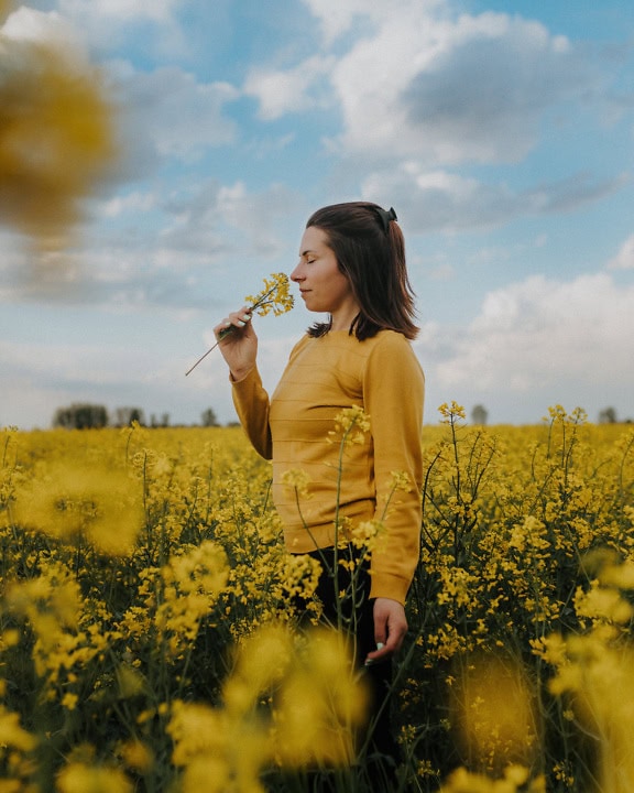 Sideportrett av en kjekk brunette kvinne som lukter en blomst i et felt med gule blomster
