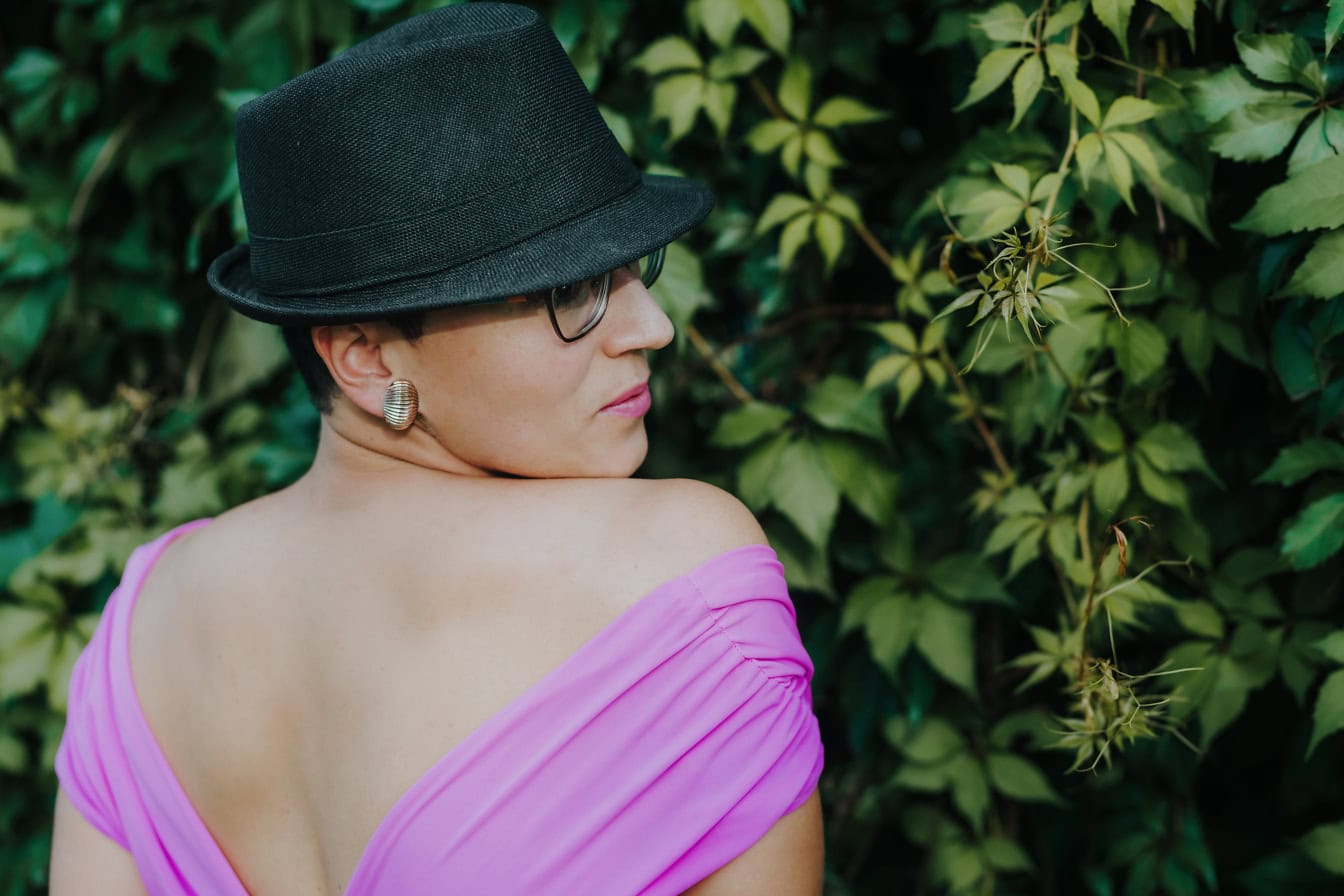 Portræt af en smuk glamourøs klædt ung kvinde iført en sort hat og lyserød rygløs kjole