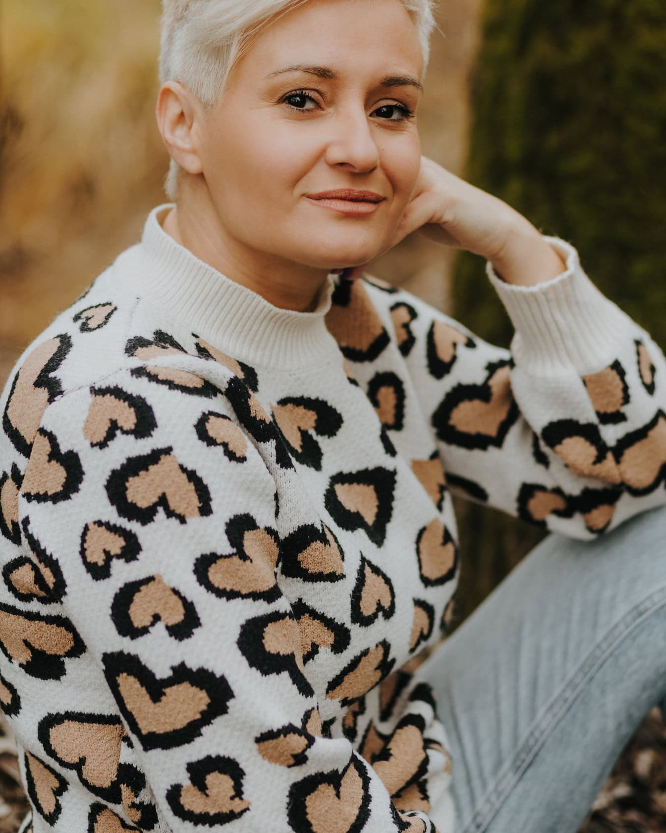 Detailní portrét blondýnky s krátkými vlasy ve svetru s leopardím vzorem a džínách