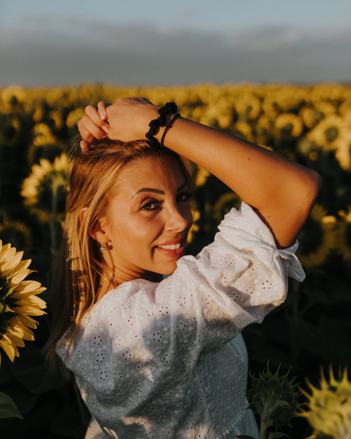 Portret wspaniałej wiejskiej blondynki na polu słoneczników z rękami we włosach