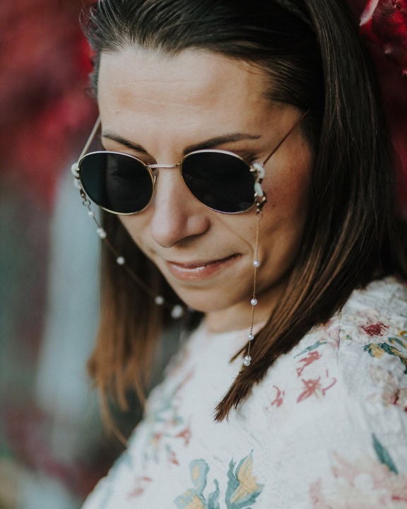 Ansigtsportræt af en ung kvinde iført solbriller i John Lennon-stil og en blomstret skjorte