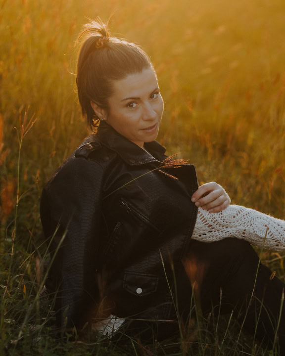 Портрет на красива брюнетка, седнала в трева в черно кожено яке
