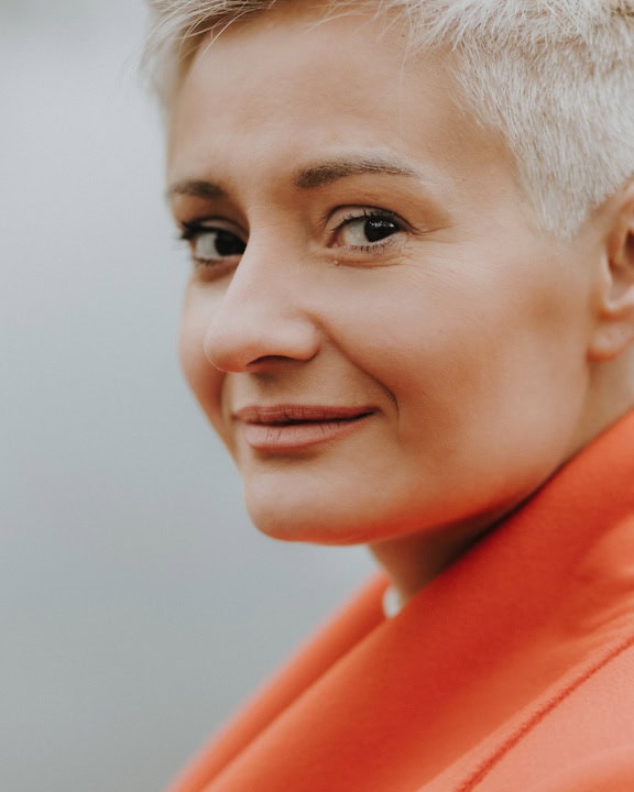 Facial portrait of a young woman with a short blonde haircut with discreet makeup in an orange jacket