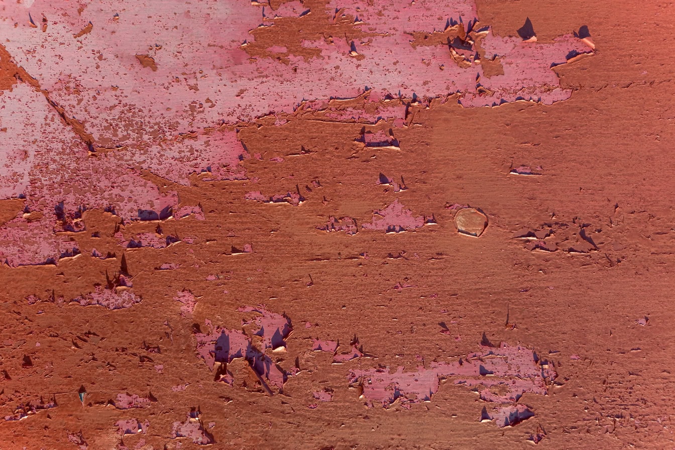 Текстура поверхности железного листа со слоями розоватой и красноватой краски, отслаивающейся от поверхности металла