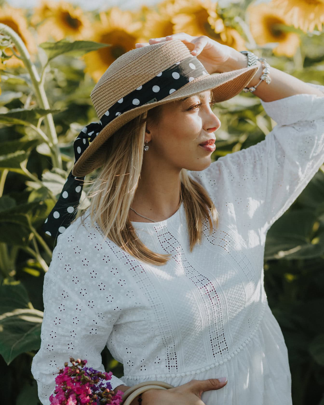 Porträtt av en ung kvinna på landet som bär en hatt i fältet av solrosor