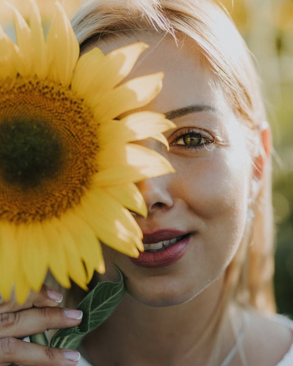一个美丽的女人的面部肖像，在她的半张脸上拿着一朵向日葵