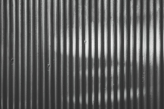 Gölgede dikey çizgiler bulunan eski paslı bir metal levhanın siyah beyaz dokusu