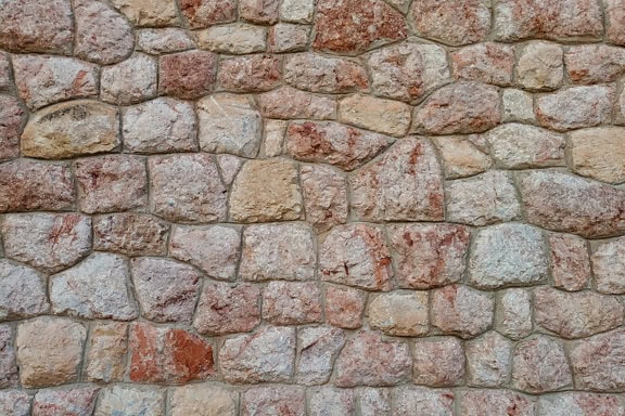 Texture of a rough stone wall made of reddish and yellowish-brown granite rocks