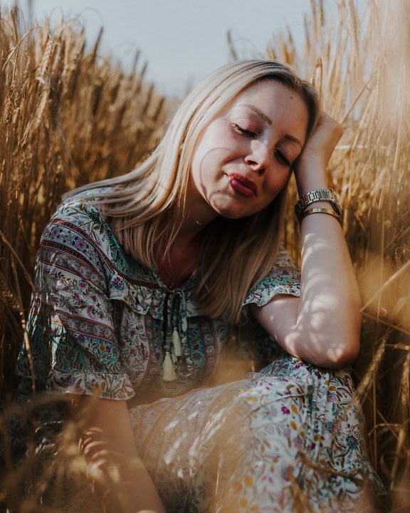 Portret młodej pięknej blondynki siedzącej na polu pszenicy i cieszącej się opalaniem