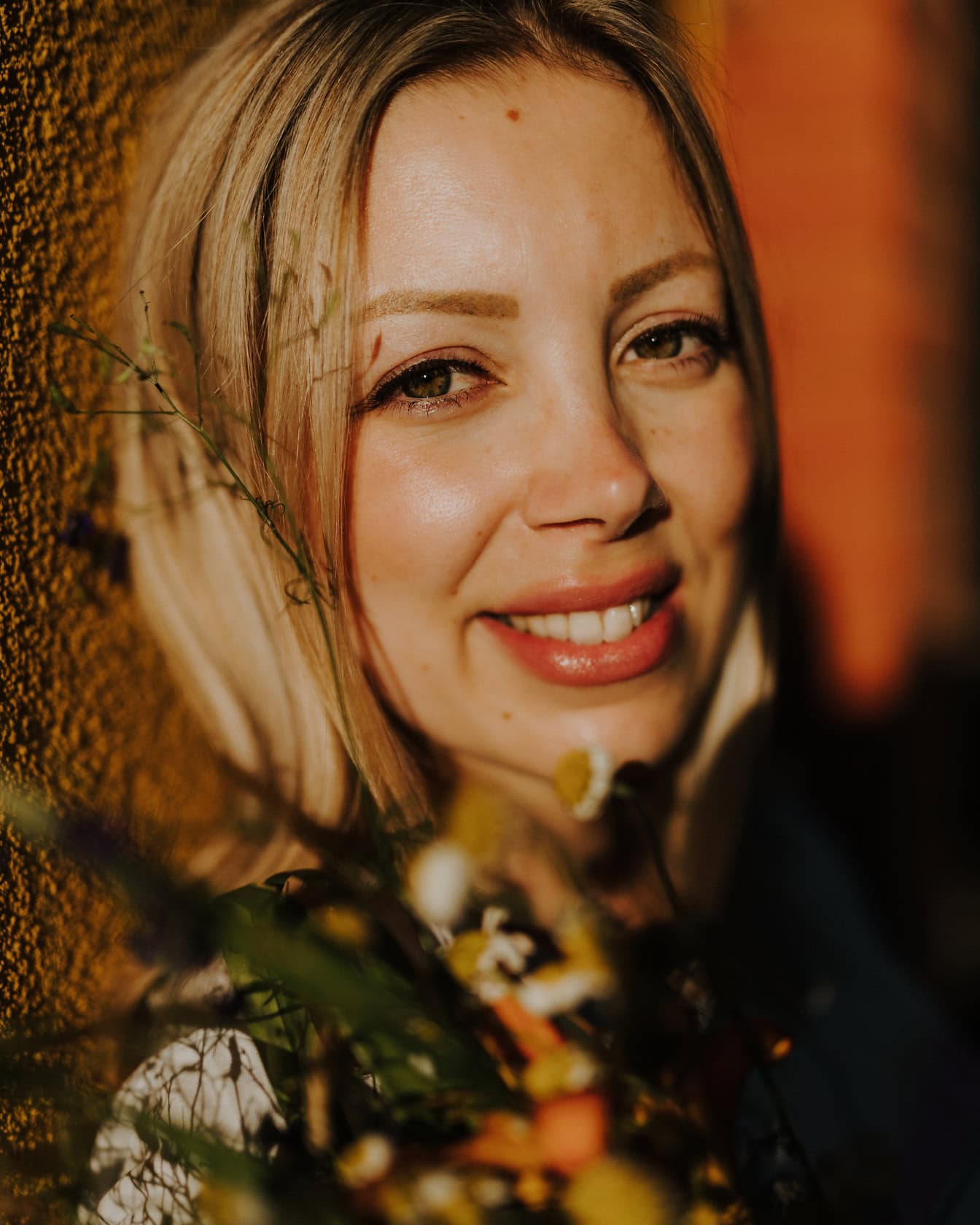 Detailný portrét usmievavej mladej ženy s blond vlasmi s kyticou kvetov