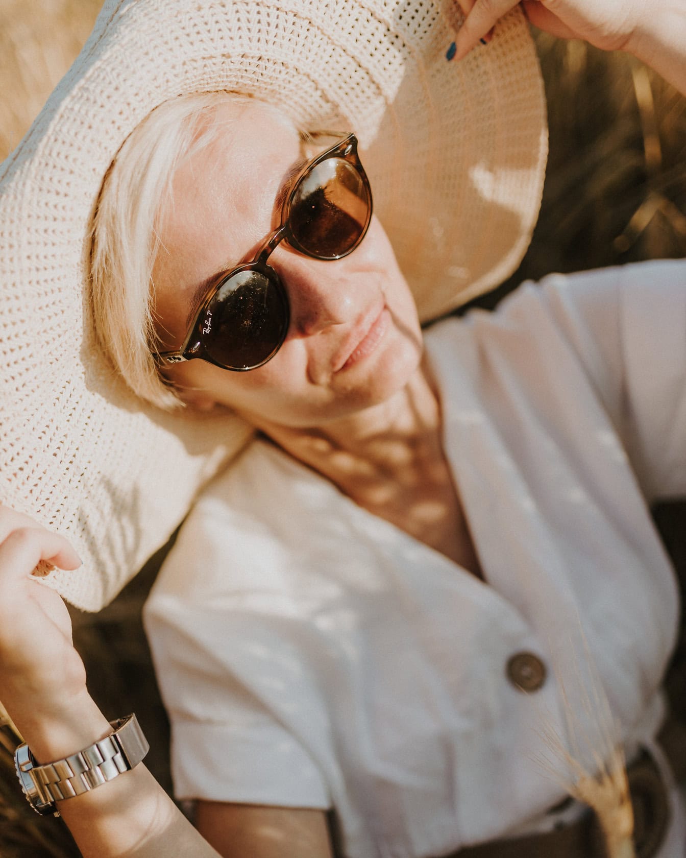 Gezichtsportret van een glamourdame die een beige hoed, witte kleding en een zonnebril draagt bij zonnige zomerdag